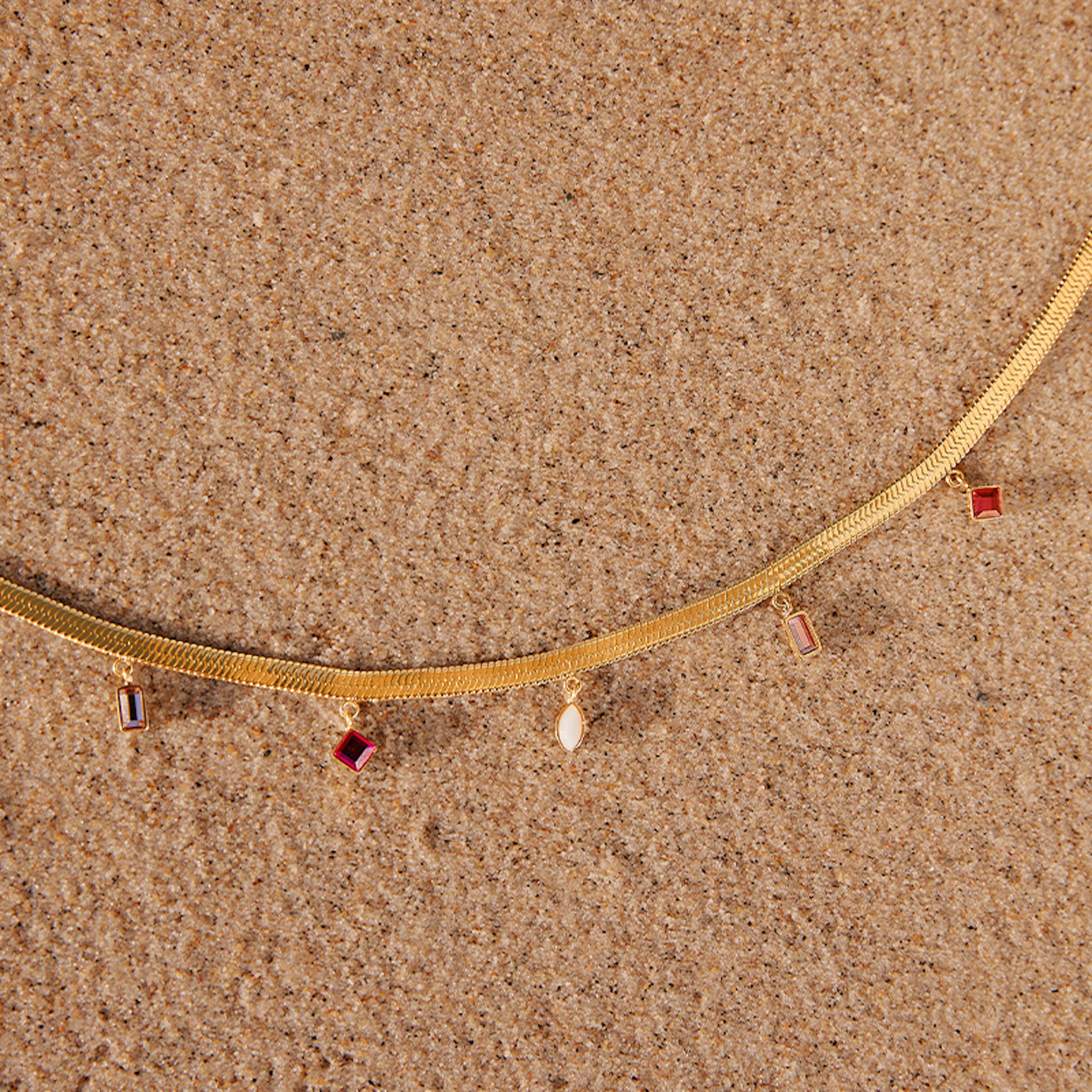 Wasserfeste Halskette mit bunten Steinchen liegt am Strand