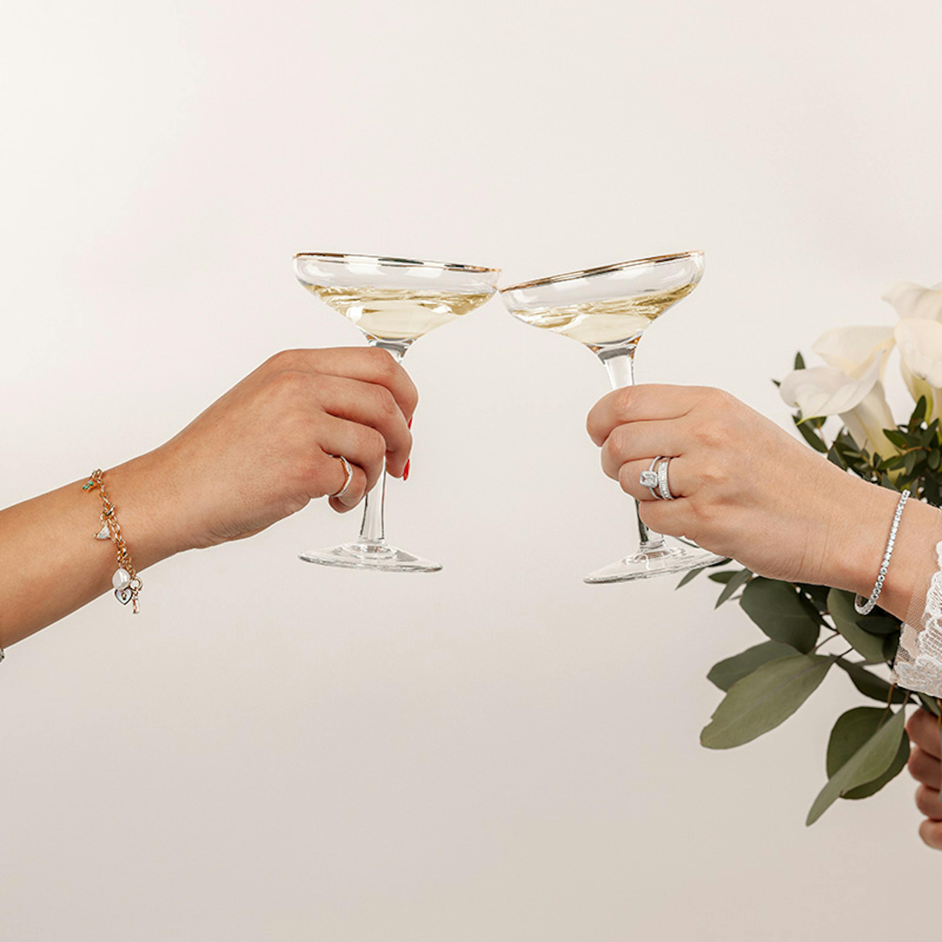 Zwei Frauen tragen funkelnde Ringe und Armbänder von Amor und stoßen auf einer Hochzeit miteinander an