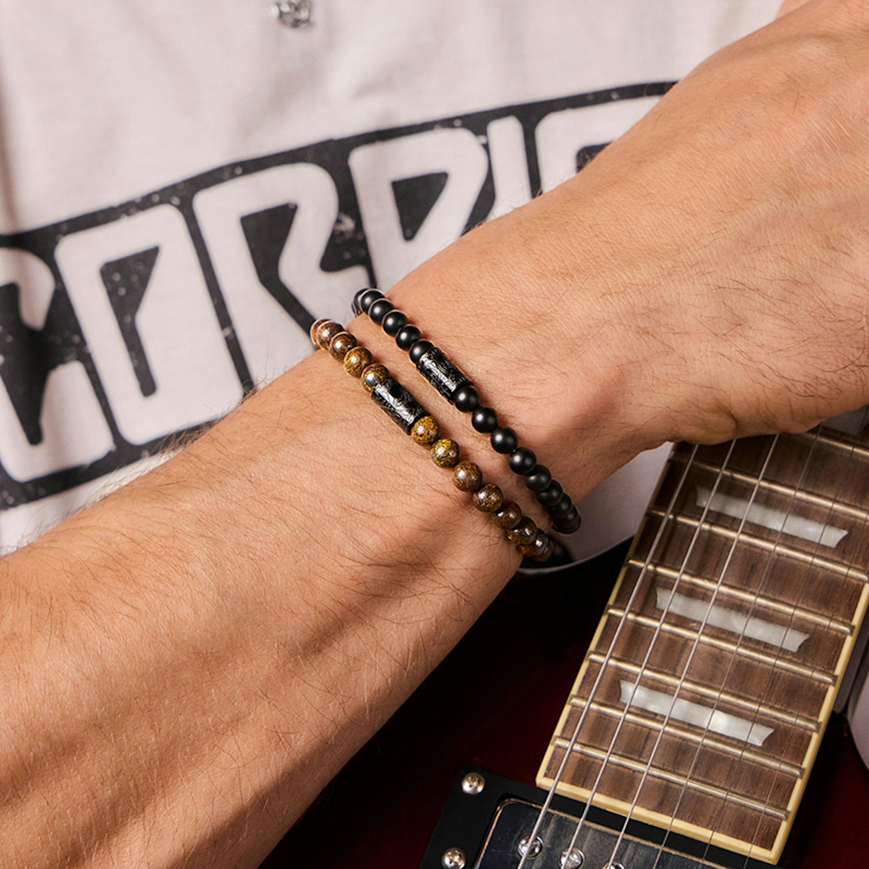 Mann trägt zwei Perlenarmbänder der neuen Scorpions Collection und hält E-Gitarre