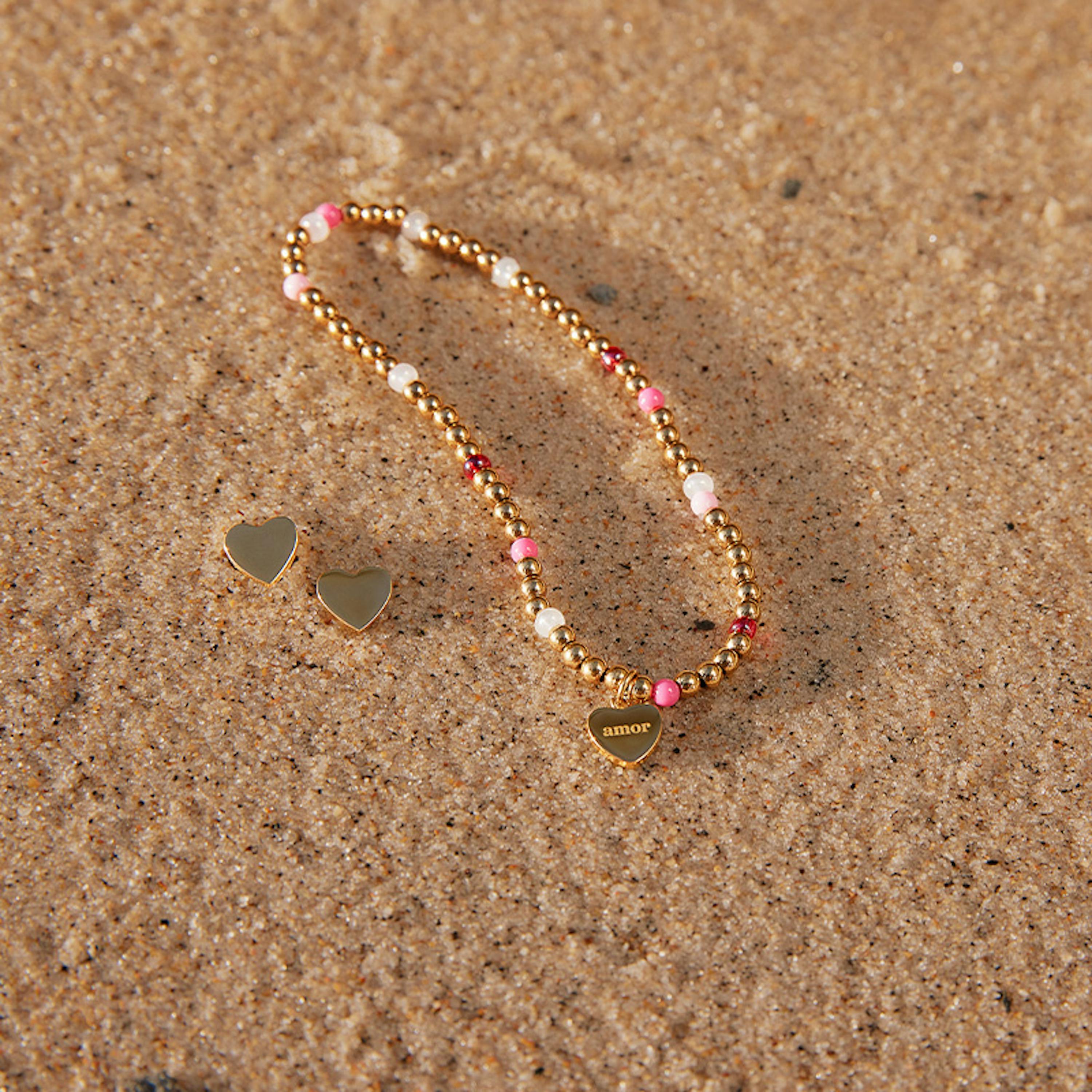 Wasserfeste goldene Ohrringe und Armband liegen am Strand